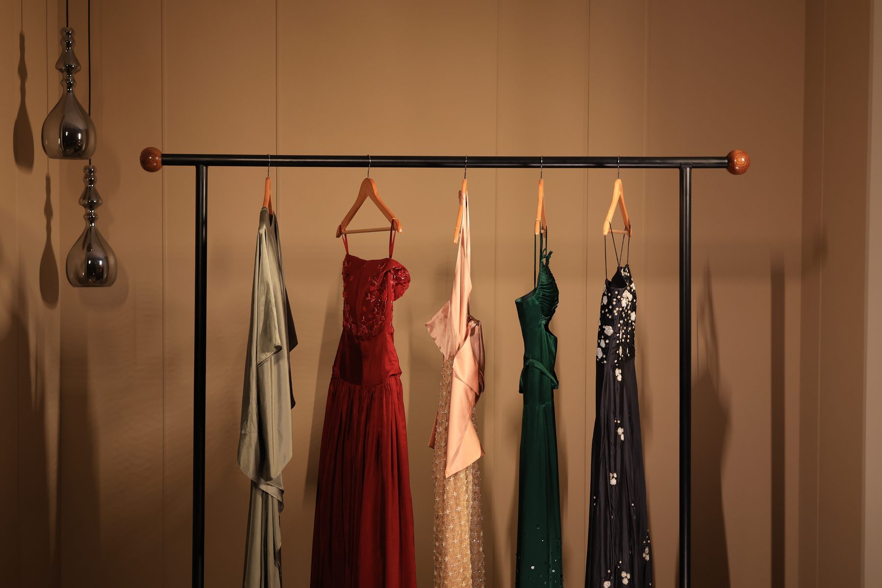 A rail of Studio Mehek occasionwear gowns in sage, red, blush, emerald and midnight